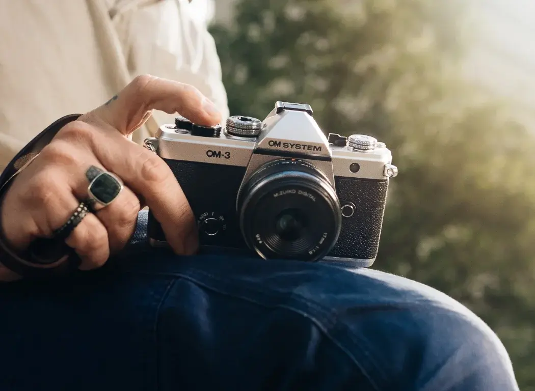 OM SYSTEM OM-3 camera in hand rested on a person leg taking a photo.